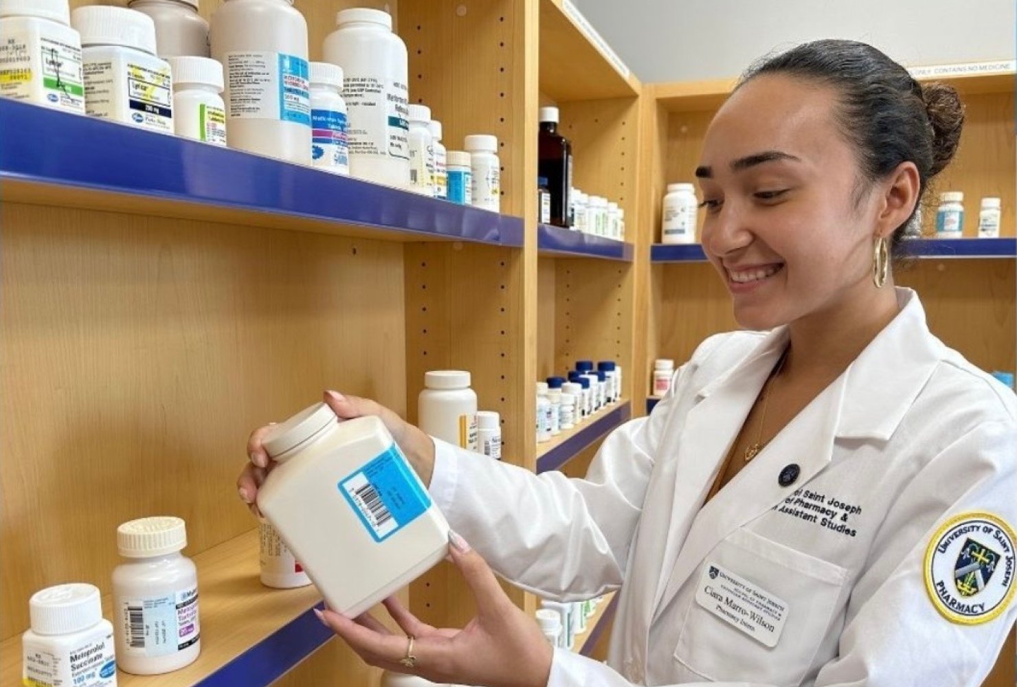 Marro-Wilson in white lab coat looking at a pill bottle.