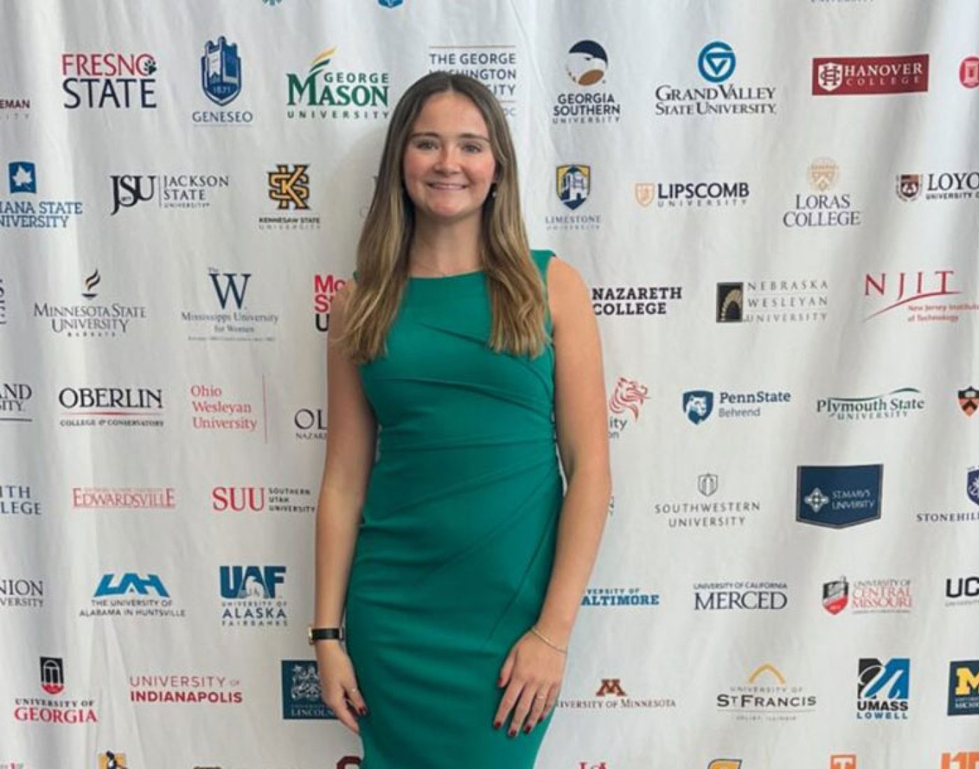 A woman in a green dress standing in front of a step and repeat