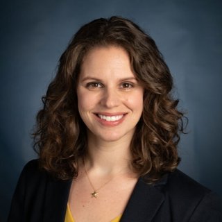 Professional headshot of Parks in yellow shirt and black cardigan.
