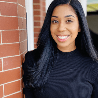 Professional headshot of Amber Newmann smiling next to a red brick wall.