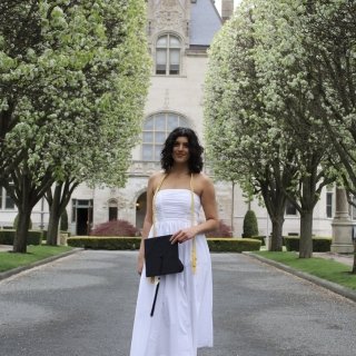 Ferreira in front of Ochre Court wearing a white dress and holding her graduation cap.