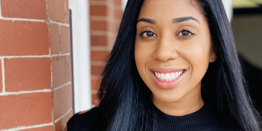 Professional headshot of Amber Newmann smiling next to a red brick wall.