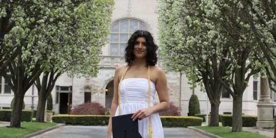 Ferreira in front of Ochre Court wearing a white dress and holding her graduation cap.