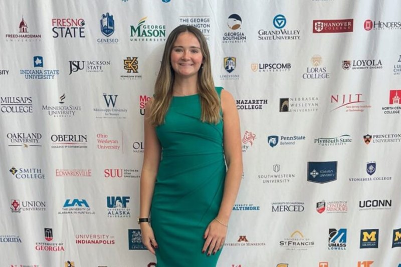A woman in a green dress standing in front of a step and repeat