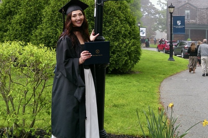 Acevedo wearing her full regalia, holding her diploma smiling next to a lamppost with Salve's logo/flag