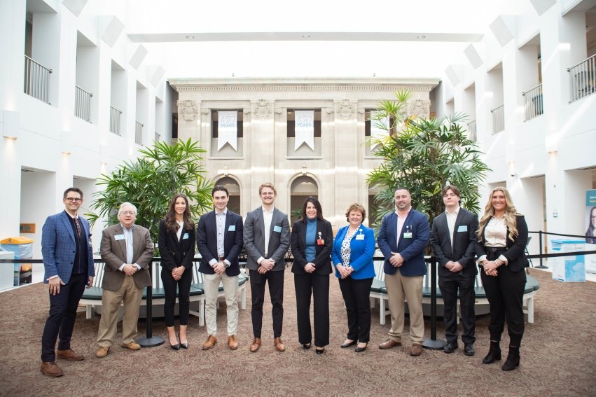 Sam Sacco and his ECN-240 students pose in 2023 with Salve alum Crista Durand, then president of Newport Hospital, to mark the release of an economic impact study the class undertook for the facility.