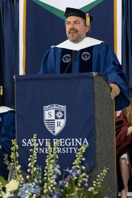 Cody Keenan in academic regalia and standing at a Salve Regina University podium, giving the keynote address.